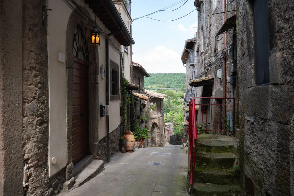 Narrow cobblestone street in an old Italian village with stone buildings, a wooden door, and a red metal railing.
