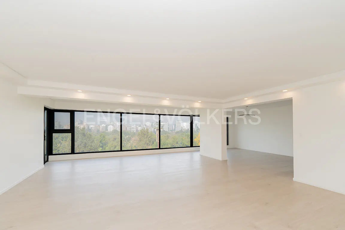 Bright, empty room with white walls, light wood floors, and a large window with a city and park view.