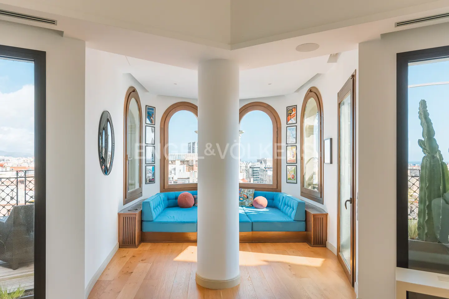 Bright room with hardwood floors, a blue sofa, and arched windows overlooking a city. A white column stands in the center.