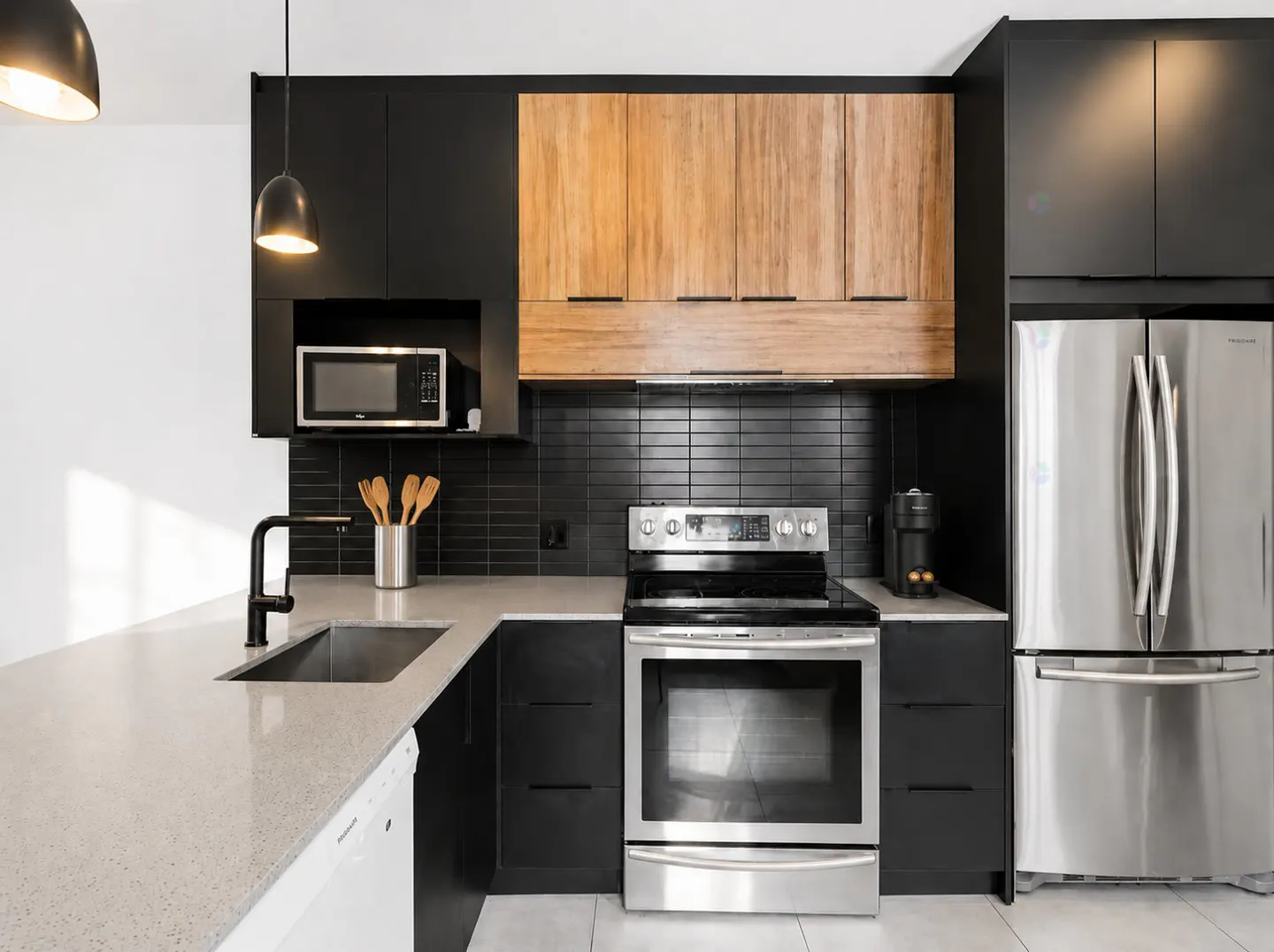 Modern kitchen with black cabinets, light wood upper cupboards, stainless steel appliances, and a quartz countertop island.