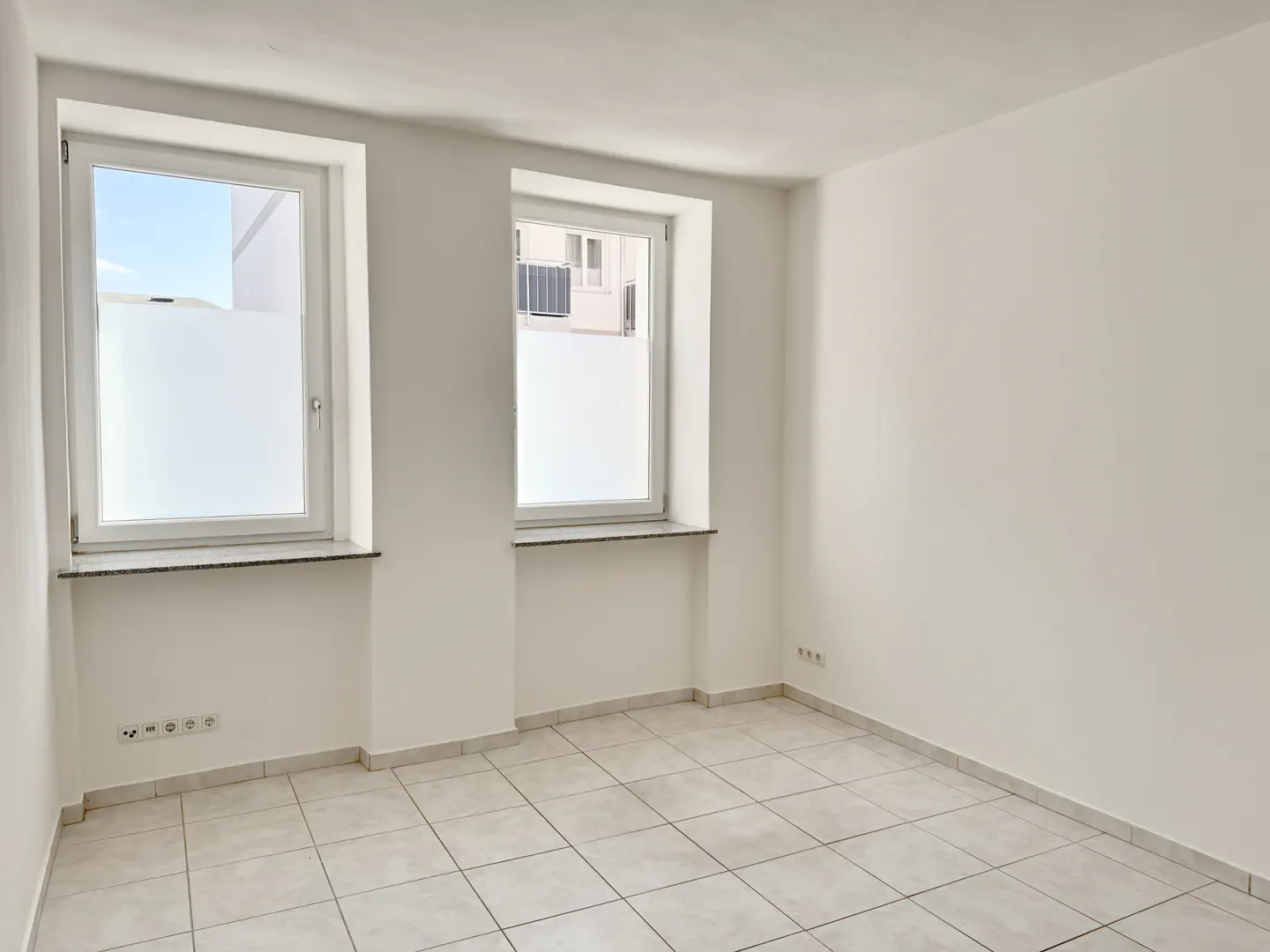 Empty room with white walls, tiled floor, and two windows with frosted privacy film.