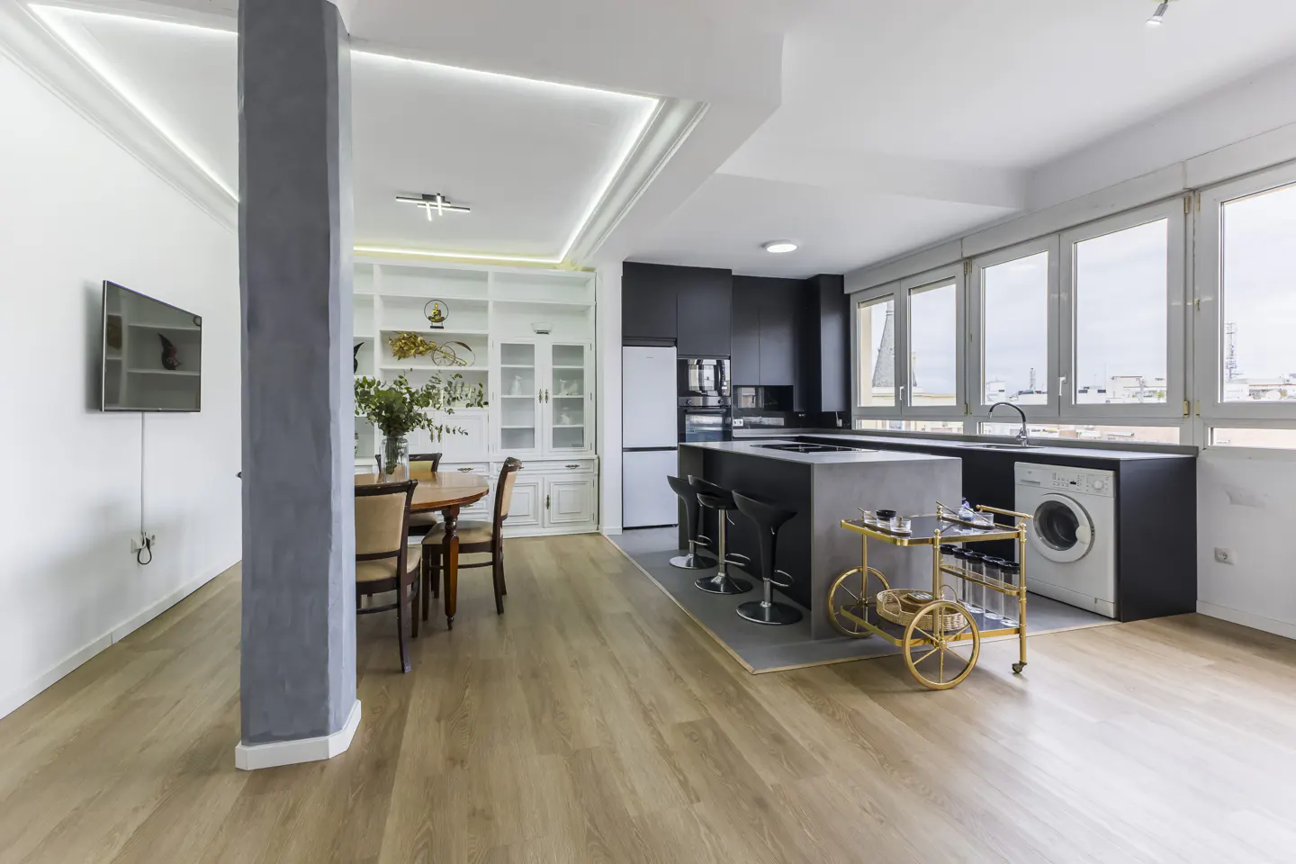 Bright, open-concept kitchen and dining area with wood floors. Features a black kitchen island, white cabinets, and a dining table with chairs.