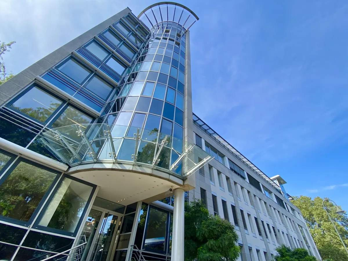 Modern office building with a curved glass facade and blue windows against a clear blue sky.