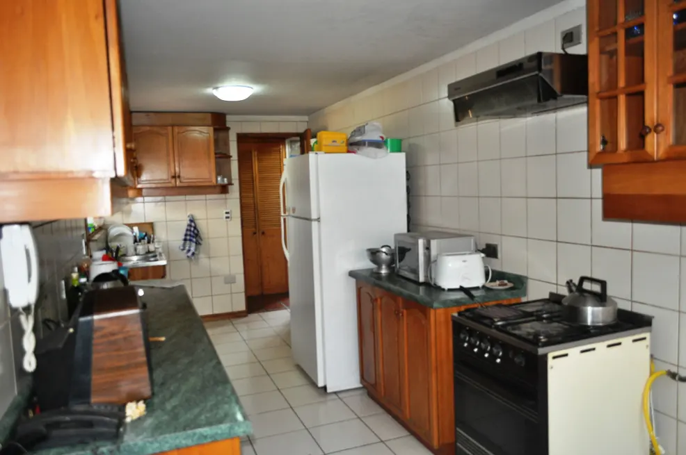 A kitchen with white tiled walls, wooden cabinets, a white refrigerator, and a black stove.