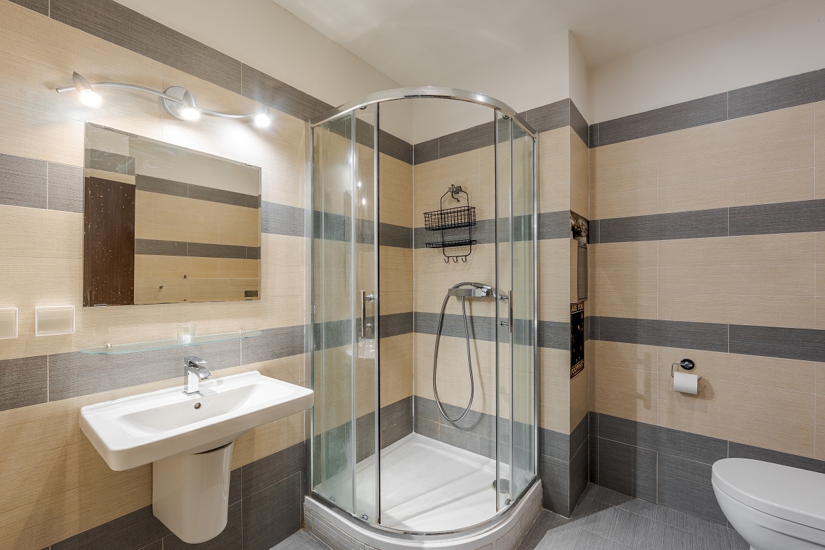 Modern bathroom with beige and gray striped tiled walls, a glass corner shower, white pedestal sink, and toilet. [AI-generated text]