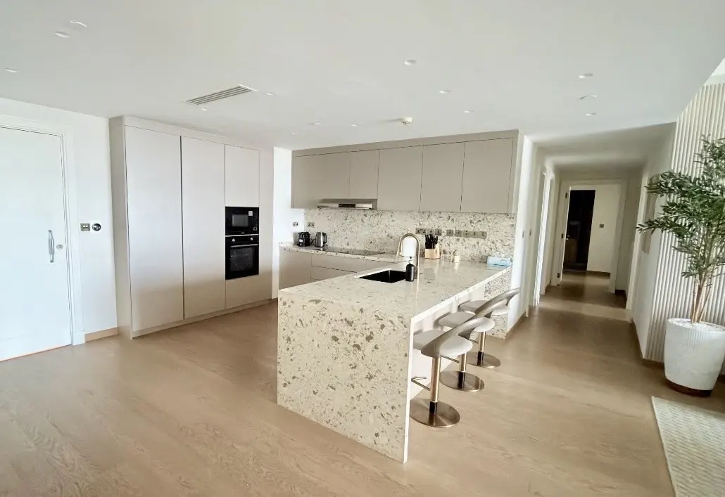 Modern kitchen with beige cabinets, terrazzo island, three bar stools, and light wood floors in an open-plan home.