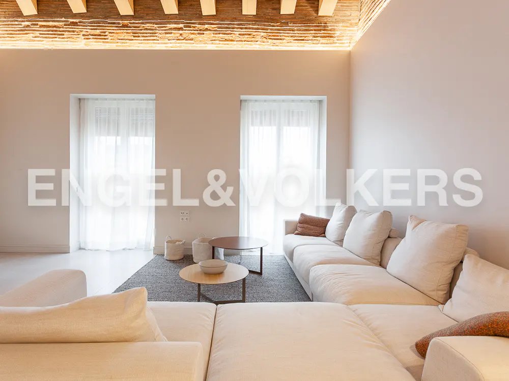Modern living room with a large beige sectional sofa, two round coffee tables, and a brick ceiling with recessed lighting.