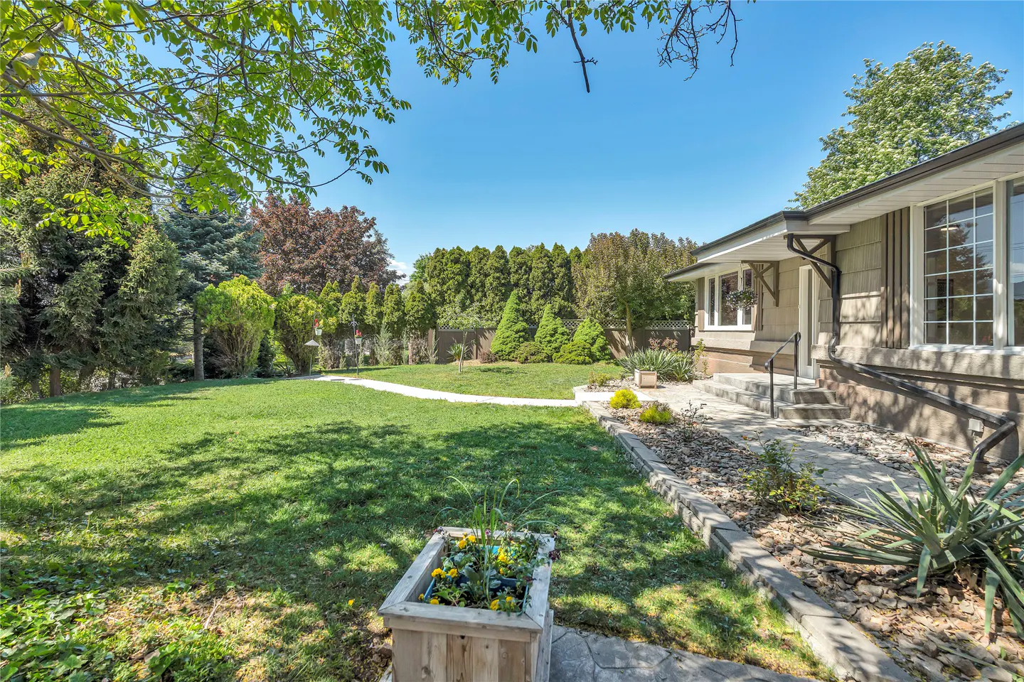 A house with a large green lawn and a stone walkway leading to the front door. Trees surround the property.
