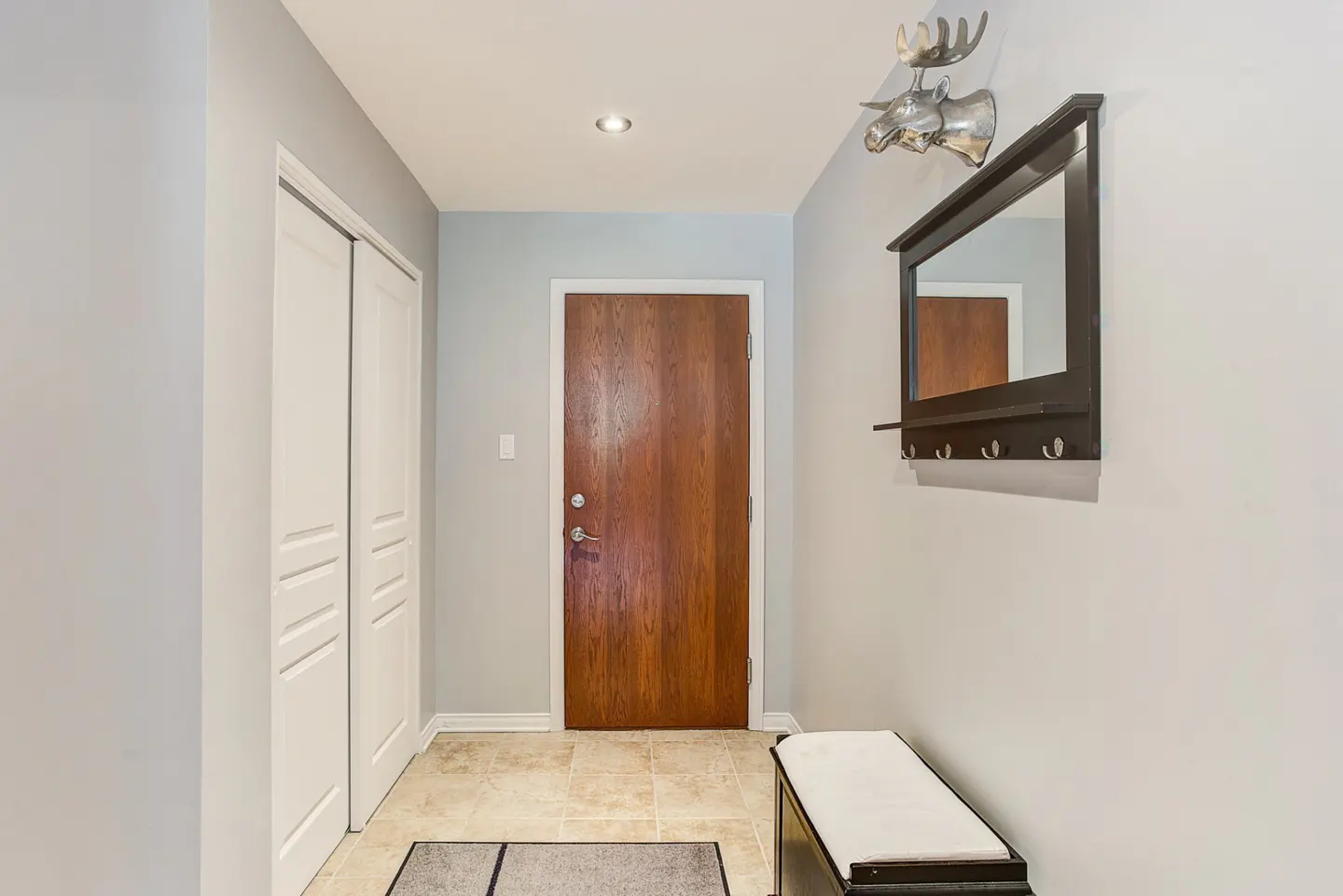 Entryway with a wood door, white closet, and a bench. A mirror with hooks and a moose head are on the wall.