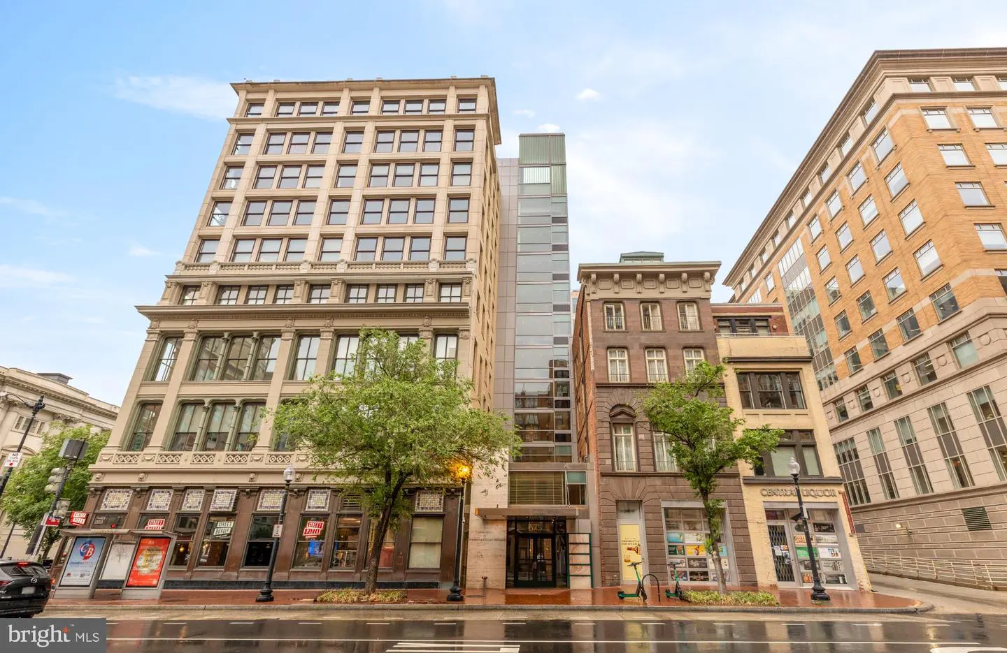 Street view of mixed-use buildings with retail and apartments on a wet city street.