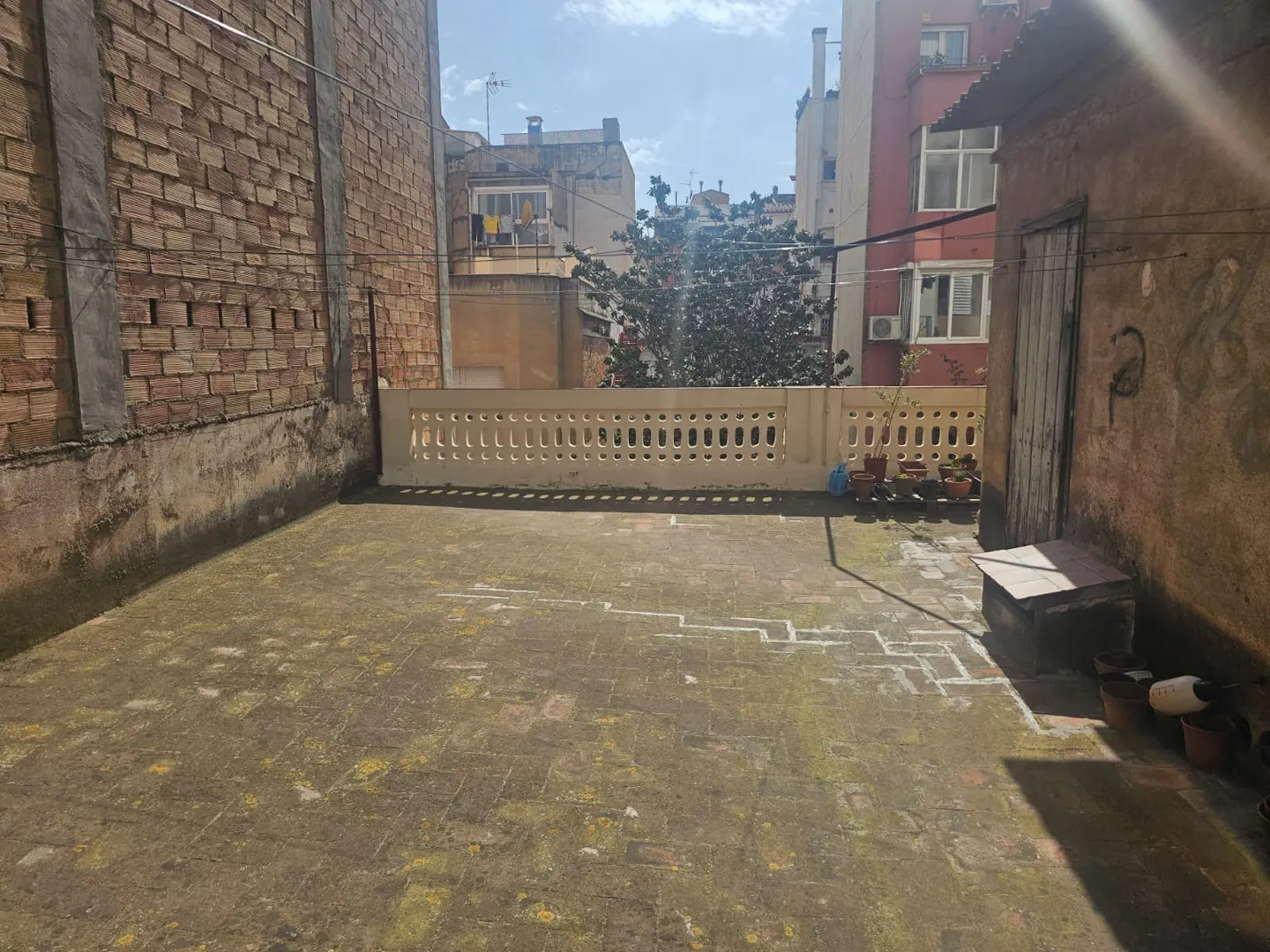 An outdoor rooftop terrace with a weathered brick floor, a decorative white balustrade, and surrounding city buildings.