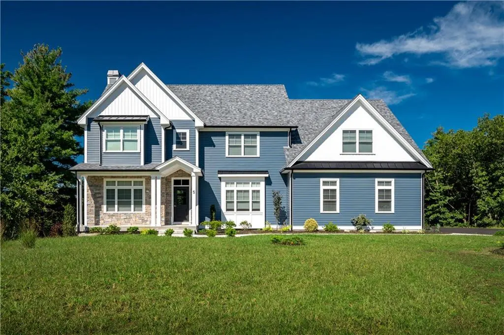 Two-story blue house with white trim, gray roof, and stone accents on a green lawn under a blue sky.