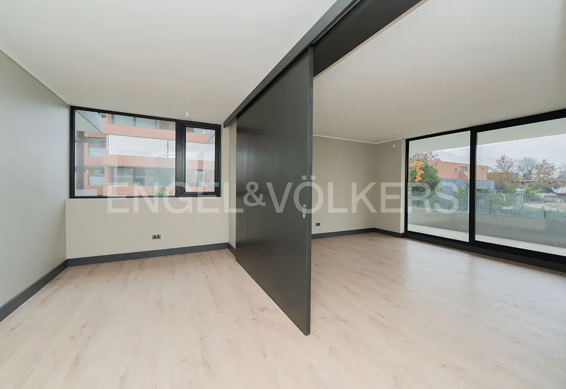 Modern room with light wood floors, beige walls, and a large black sliding door separating two bright living spaces.