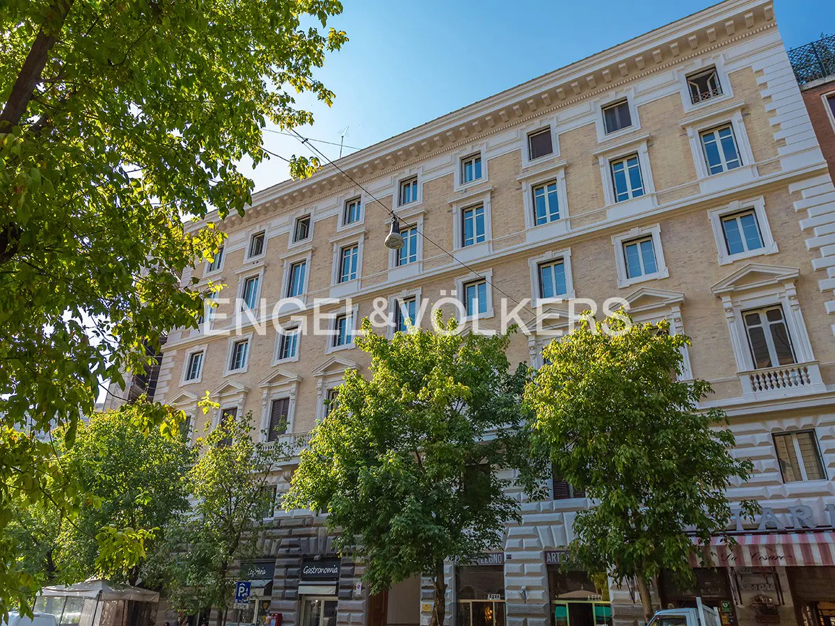 Exterior view of a multi-story, light-yellow building with many windows, trees, and the Engel & Völkers logo.