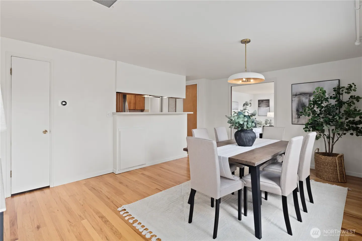 Dining room with a wooden table, six beige chairs, a modern pendant light, and a potted plant on a white area rug.
