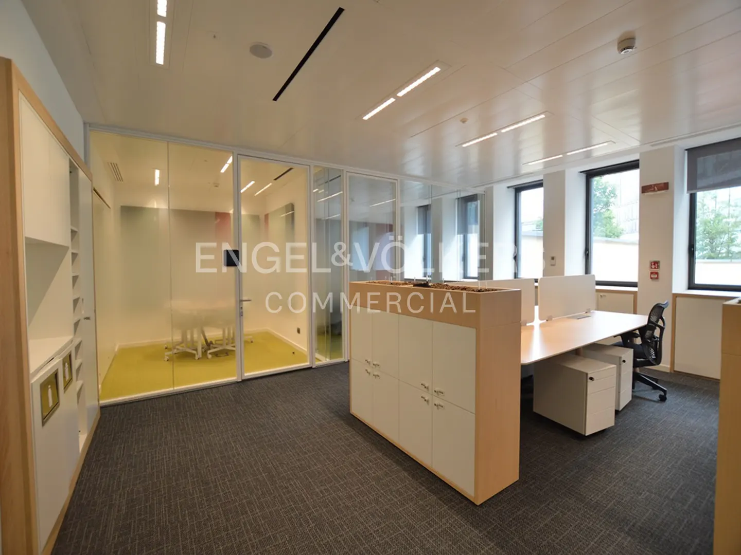 Bright office space with desks, chairs, and a glass-walled conference room with yellow carpet.