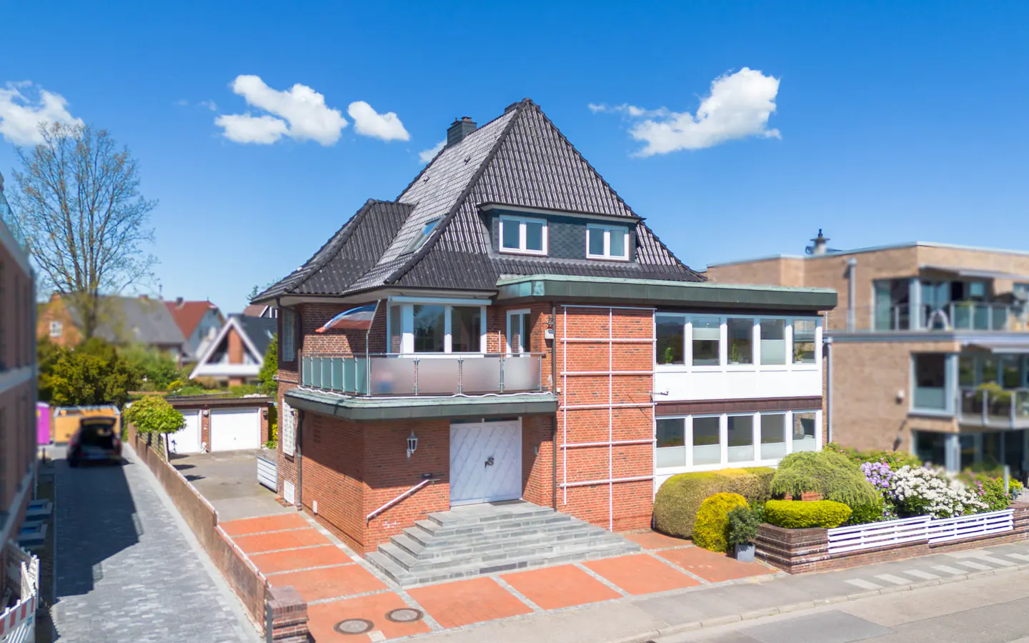 A two-story brick house with a dark roof, white trim, and a small balcony on a sunny day.
