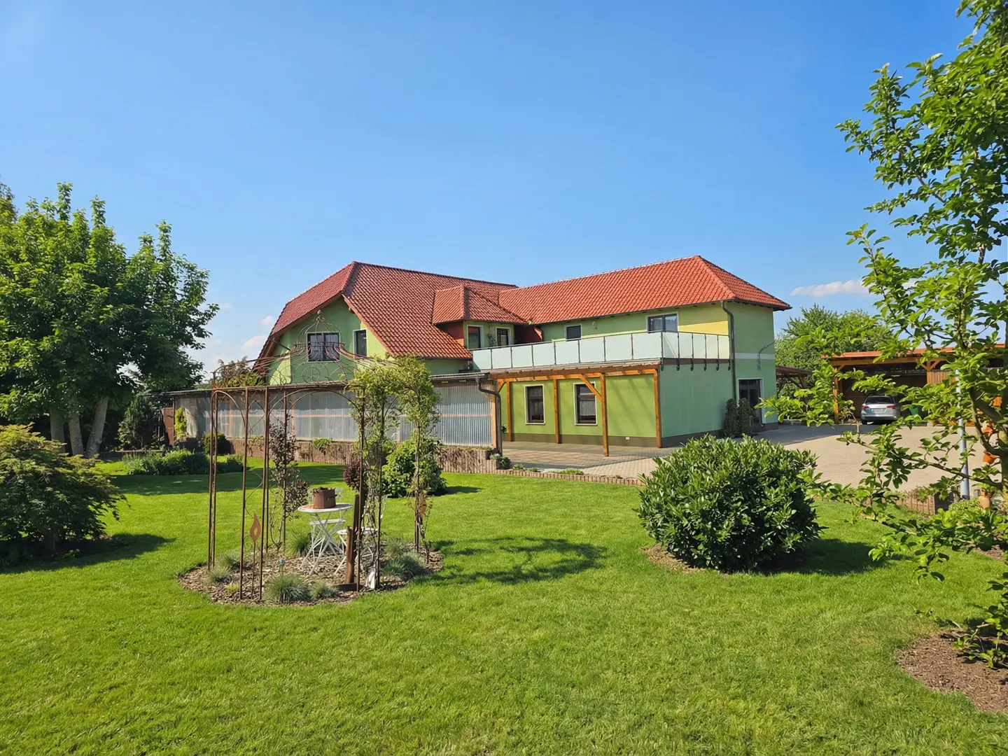 Exterior of a two-story green house with a red roof, a well-manicured lawn, and a blue sky.