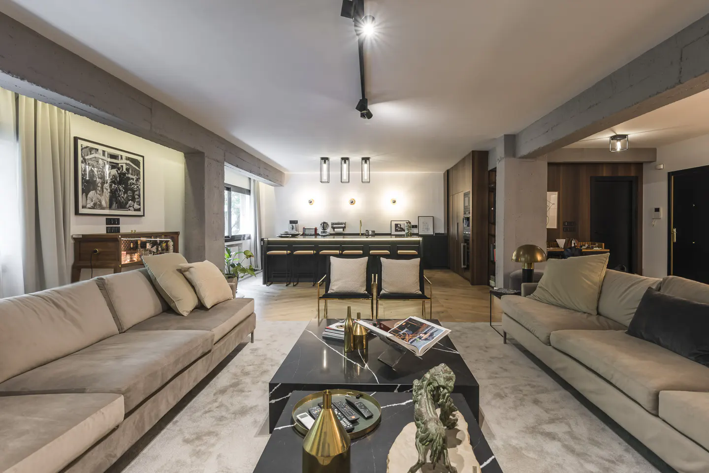 A modern living room with two beige sofas, a black marble coffee table, and an open kitchen with a black island.