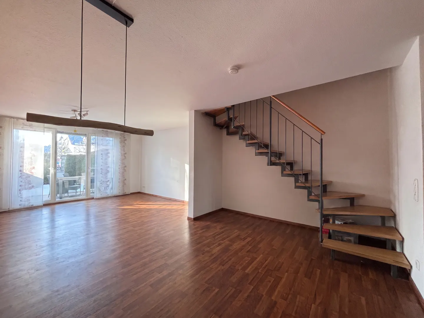 Open-plan living room with wood floors, a modern floating staircase, and a unique wooden pendant light fixture.