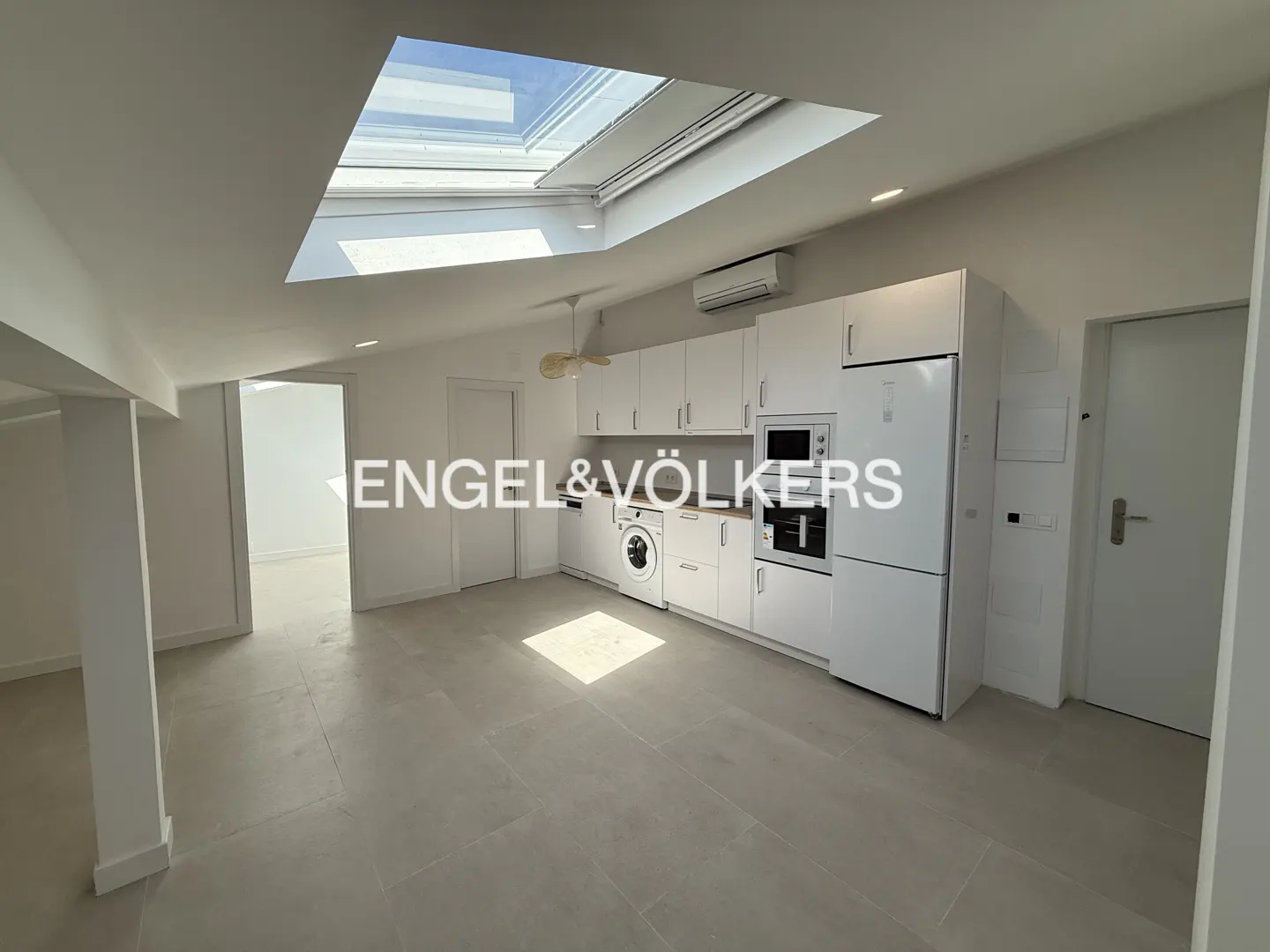 Bright, modern kitchen with white cabinets, appliances, and a skylight. Gray tile floor and white walls.