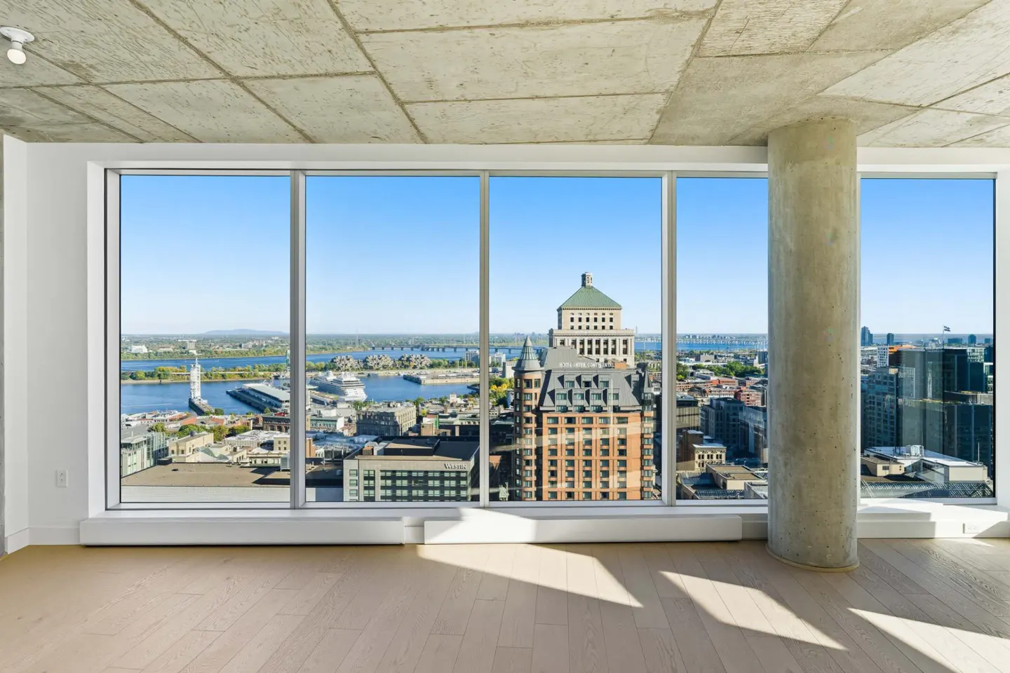 Bright, empty room with a large window view of Montreal's skyline, river, and buildings on a sunny day.