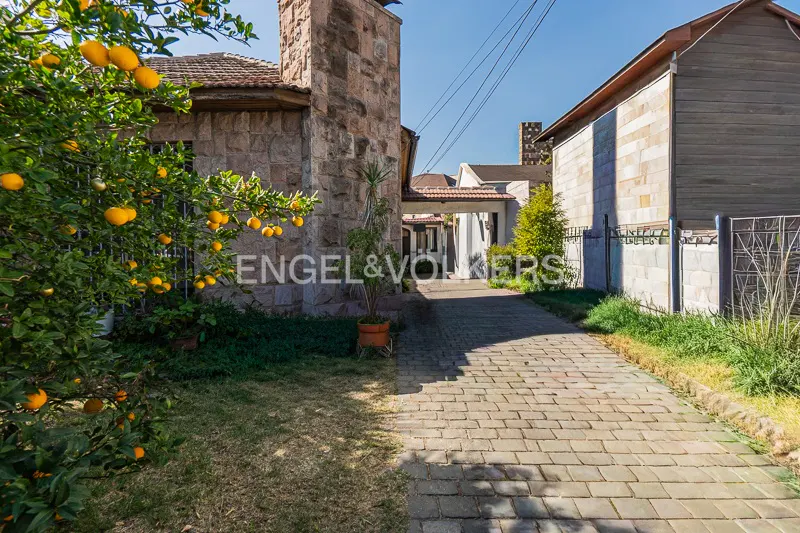Exterior view of a stone house with a brick driveway, a tree with oranges, and the Engel & Volkers logo.