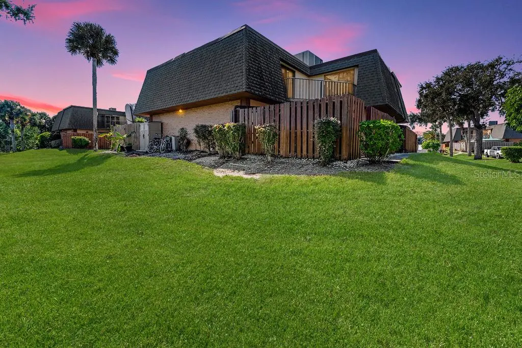 Two-story townhouse with a dark shingled roof and wooden fence, set against a vibrant pink and purple sunset sky.