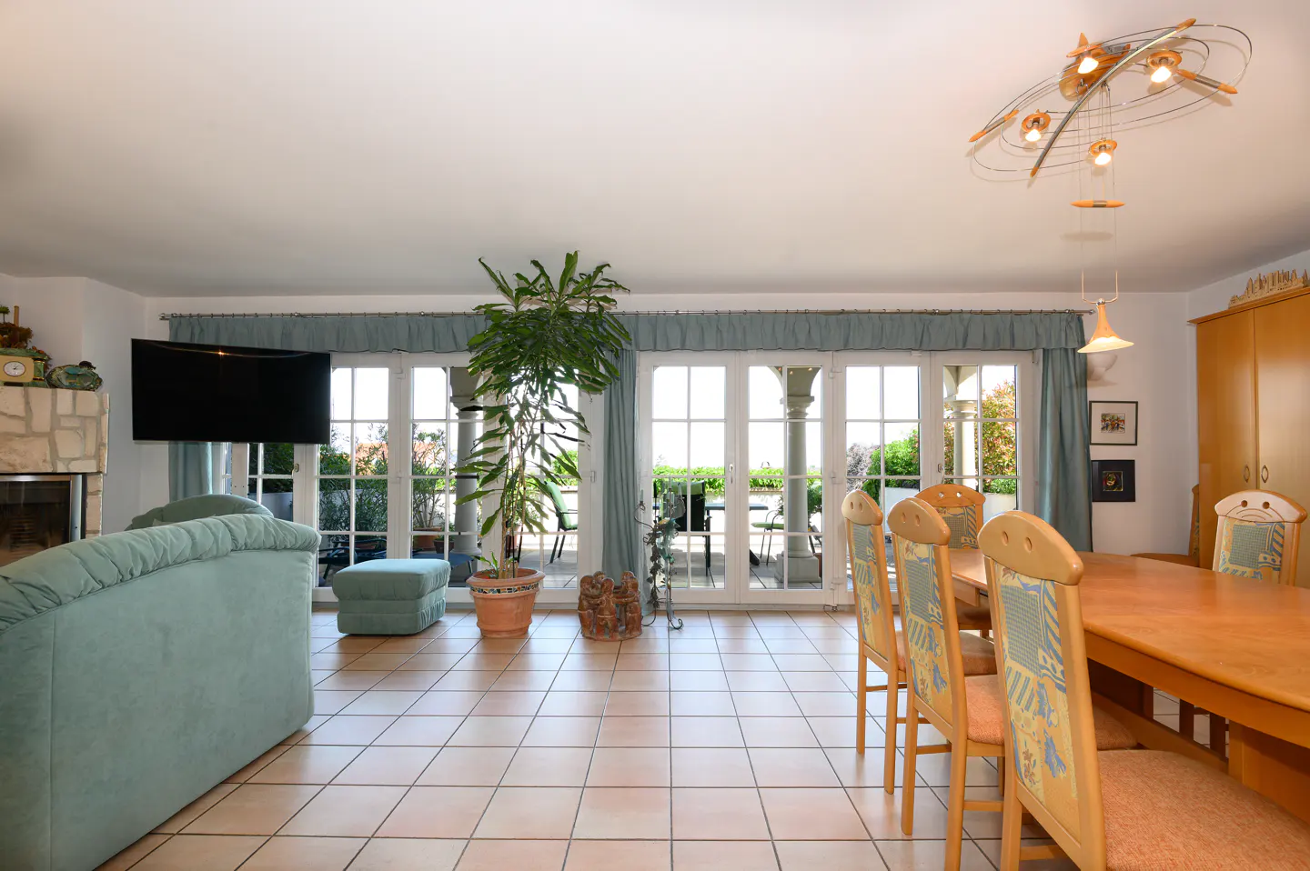 Bright living room with tile floor, light blue sofa, dining table with chairs, and French doors to a patio.