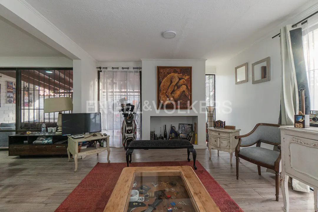 Living room with wood floors, a red rug, a glass-top coffee table, a fireplace with art, and vintage-style furniture.