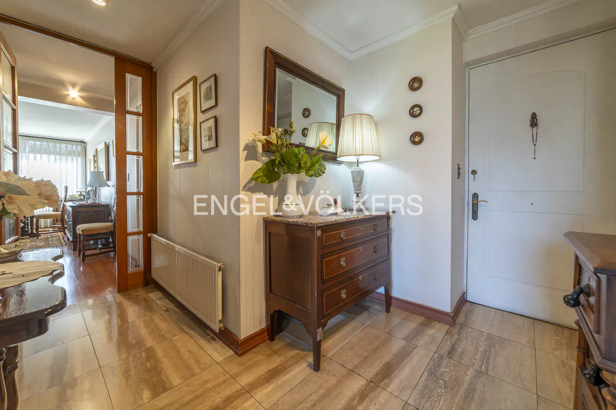 A home's entryway with a wooden dresser, mirror, and a white door. The floor is tiled in a light brown color.