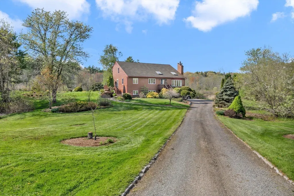A two-story red brick house with a long gravel driveway and green lawn under a blue sky.