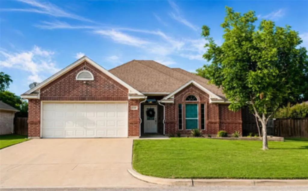 A single-story brick house with a white garage door, green lawn, and blue sky.