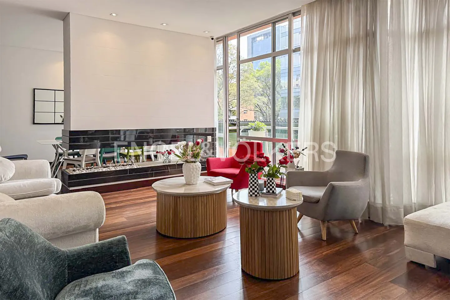 Modern living room with hardwood floors, a black fireplace, two round wooden coffee tables, and red and grey armchairs.