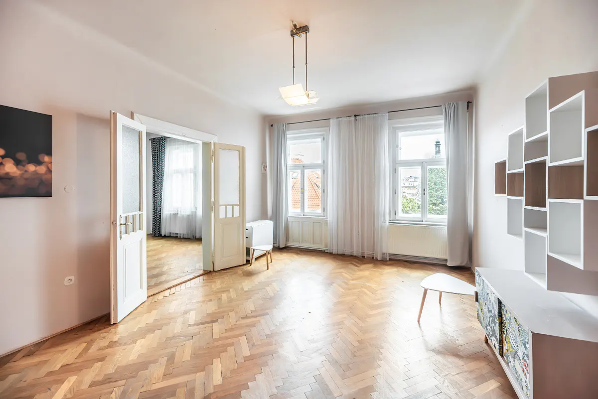 Bright living room with herringbone wood floors, white walls, modern shelving, and a doorway leading to another room.