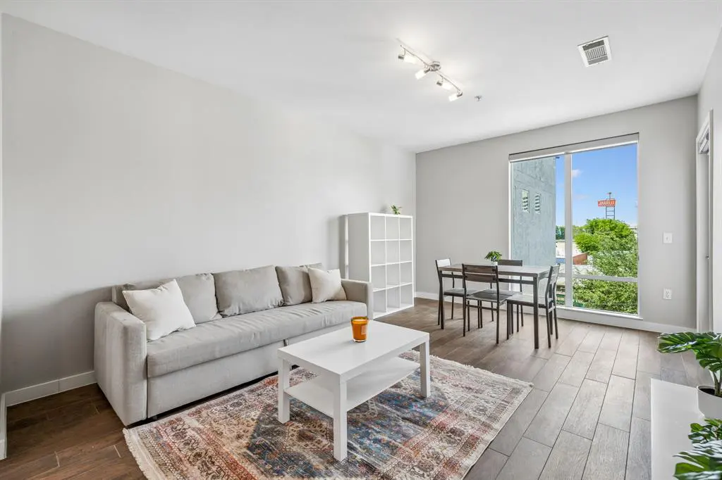 Living room with a gray sofa, white coffee table, and dining set near a large window with a city view.