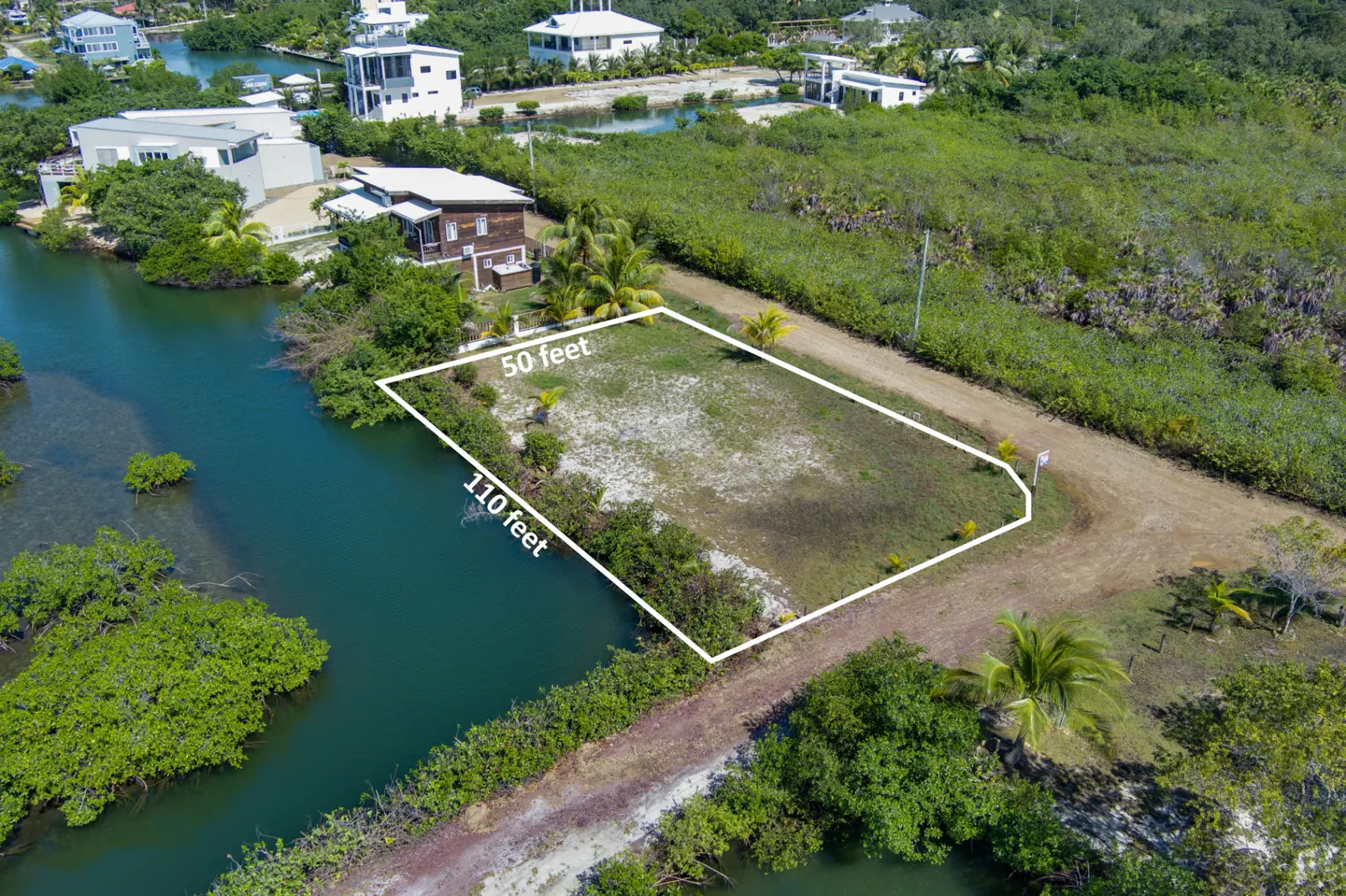Aerial view of a vacant lot outlined in white, measuring 50x110 feet, next to a canal and lush green vegetation.
