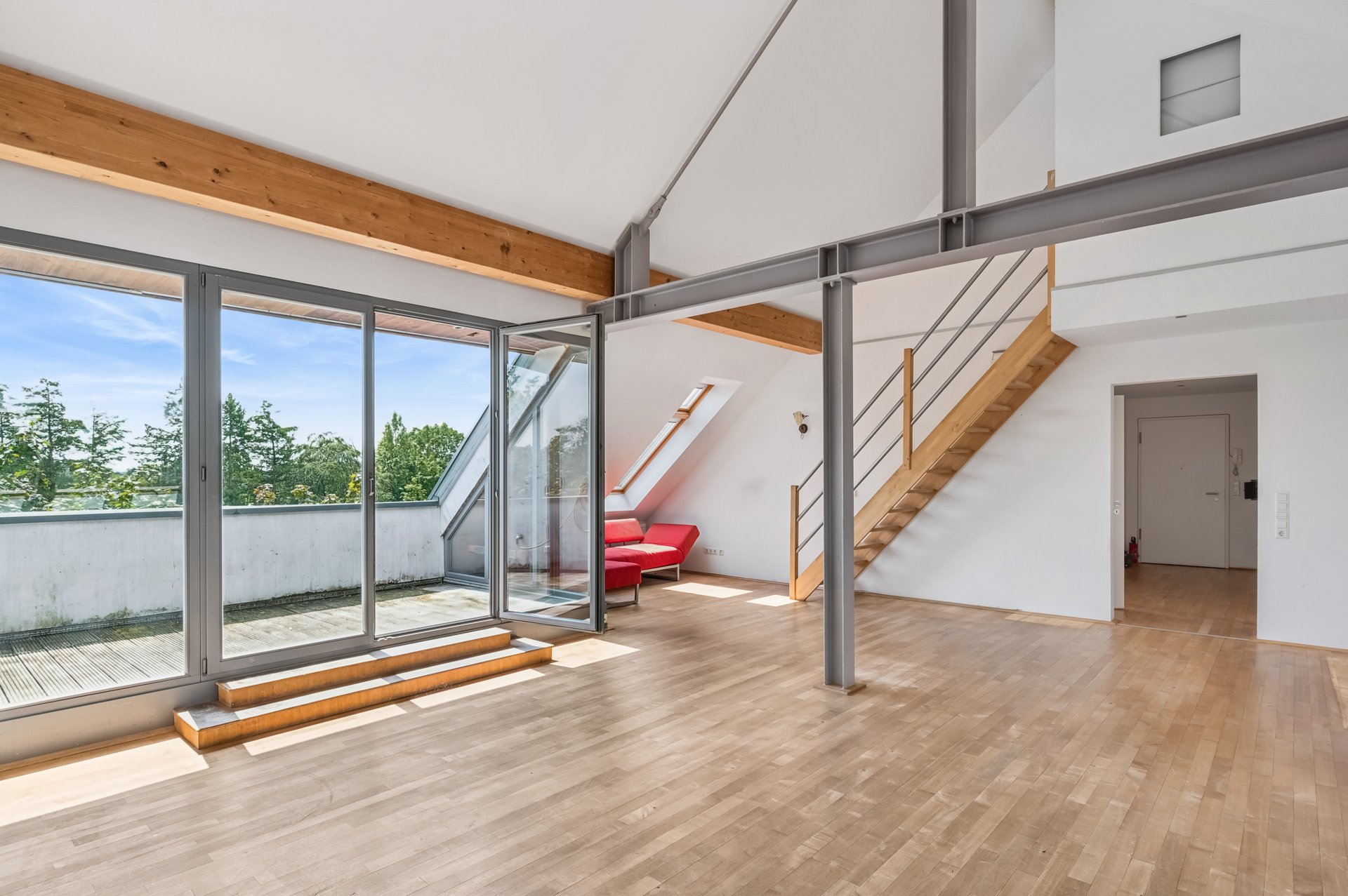 Modern loft with hardwood floors, high ceilings, steel beams, a wooden staircase, and glass doors opening to a balcony. [AI-generated text]