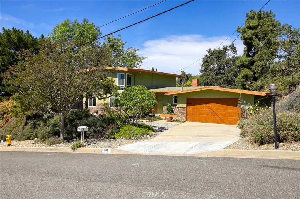 Two-story green house with a brown garage door and a concrete driveway on a sunny day.