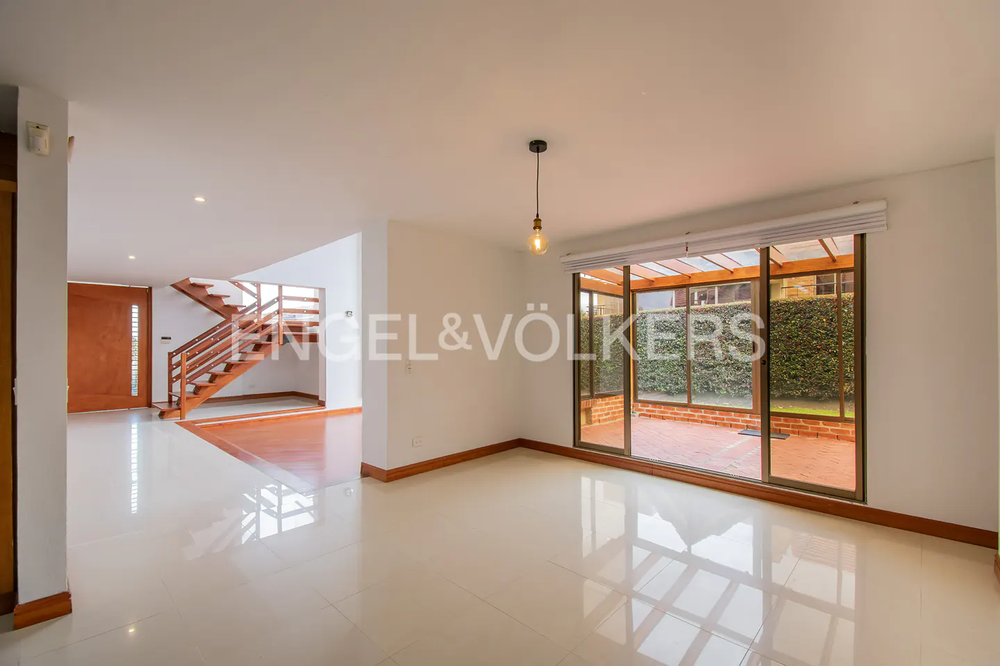 Bright, open living area with white tile floors, a wooden staircase, and large glass doors leading to a patio.