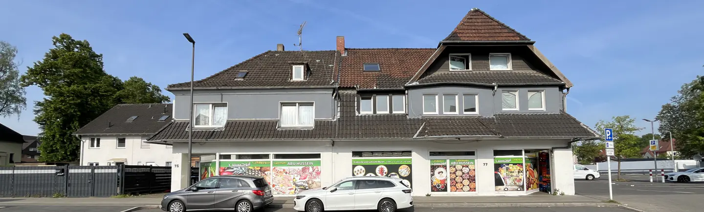 Two-story gray building with a store front. Cars are parked in front of the building. The sky is blue.