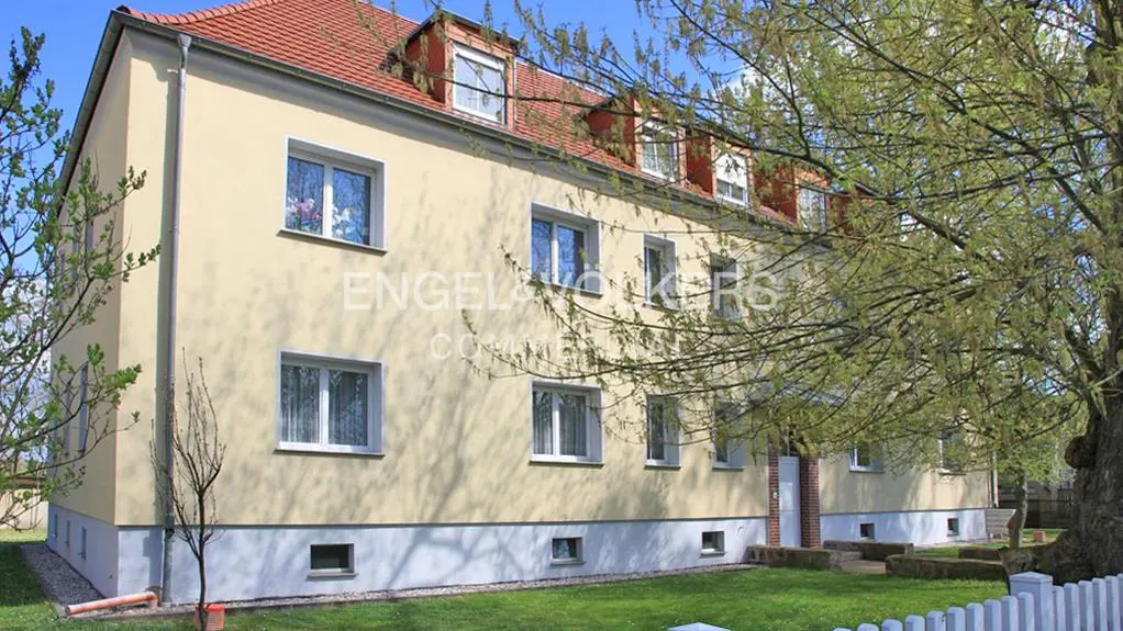 Exterior view of a multi-story, light yellow building with a red tile roof and white-framed windows, surrounded by green lawn and trees.