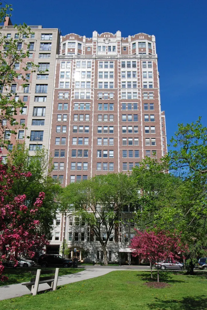 A tall brick apartment building with white trim, viewed from a green lawn with trees under a blue sky.