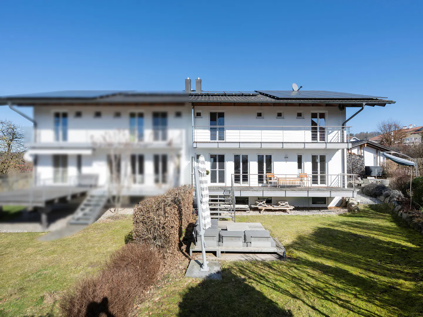 Two-story white house with balconies, solar panels, and a green lawn on a sunny day.