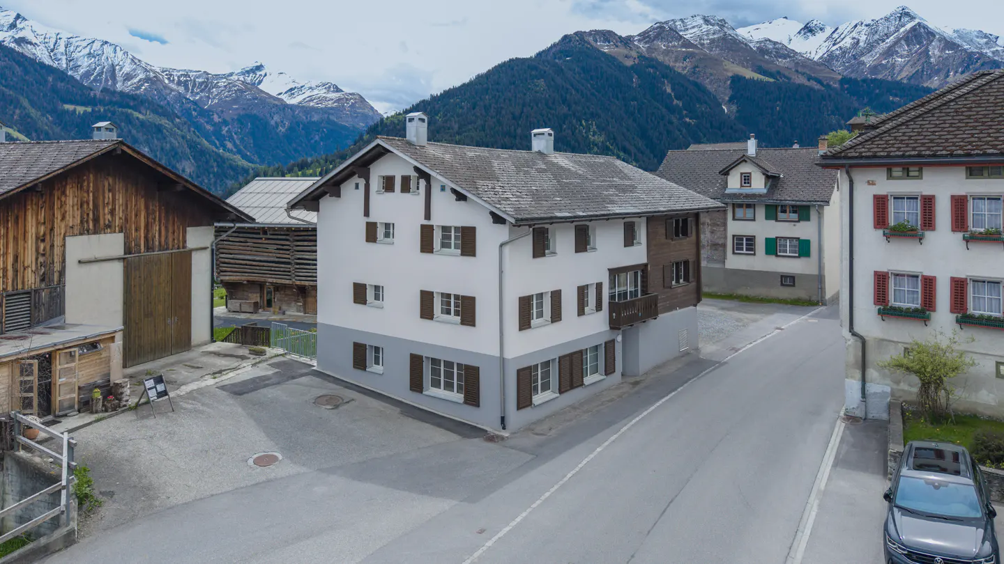 Exterior of a white two-story house with brown shutters, set against a backdrop of snow-capped mountains.