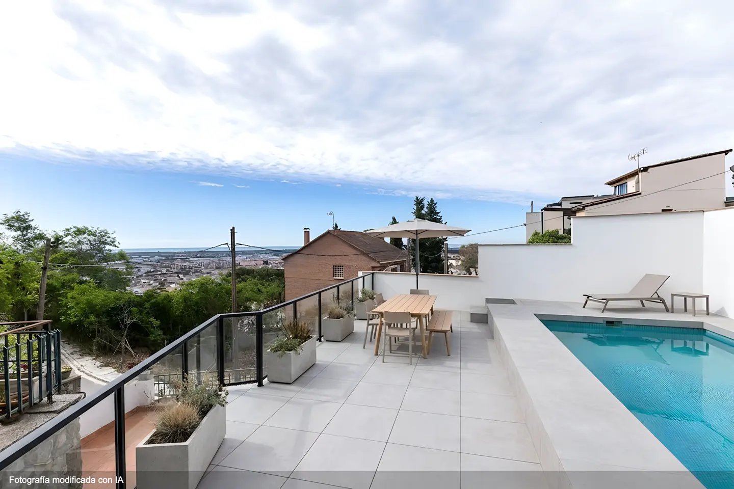 Rooftop patio with a pool, table, chairs, and lounge chair. City view in the background. Blue sky with clouds.