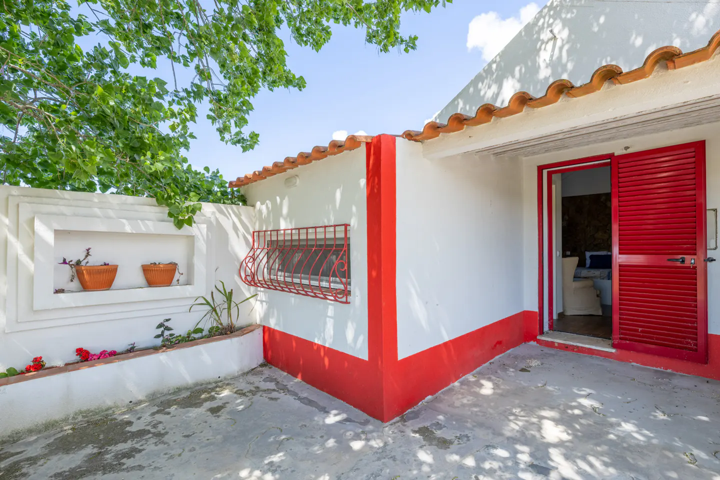 Exterior view of a white building with red trim, a red shuttered door, and potted plants.