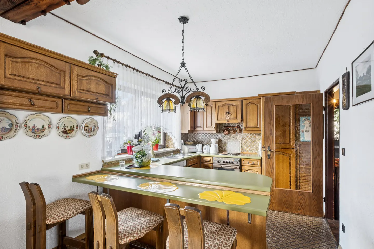 A kitchen with wood cabinets, a green countertop bar, and decorative plates on the wall.