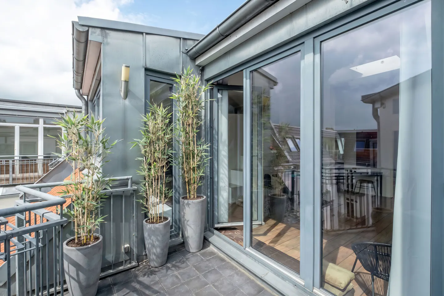 A modern balcony with gray tile flooring, potted bamboo plants, and large sliding glass doors.