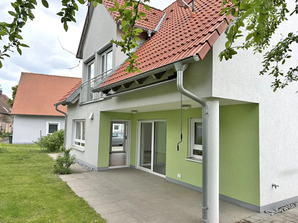 Exterior view of a two-story house with a red tile roof, light green walls, and a patio with sliding glass doors.